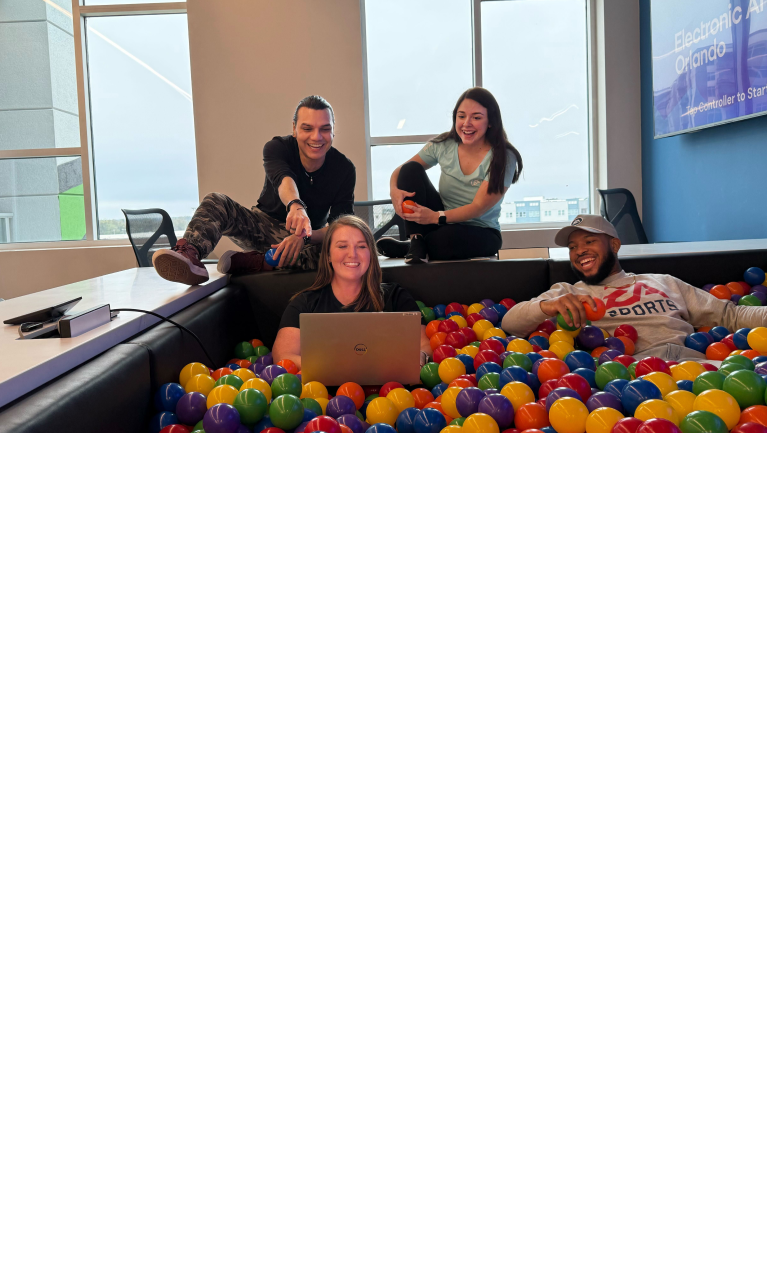 Four happy colleagues are sitting together and working in a ball pit in an office space.